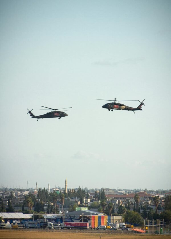 Two military helicopters hover above a city, offering a striking scene against the open sky.